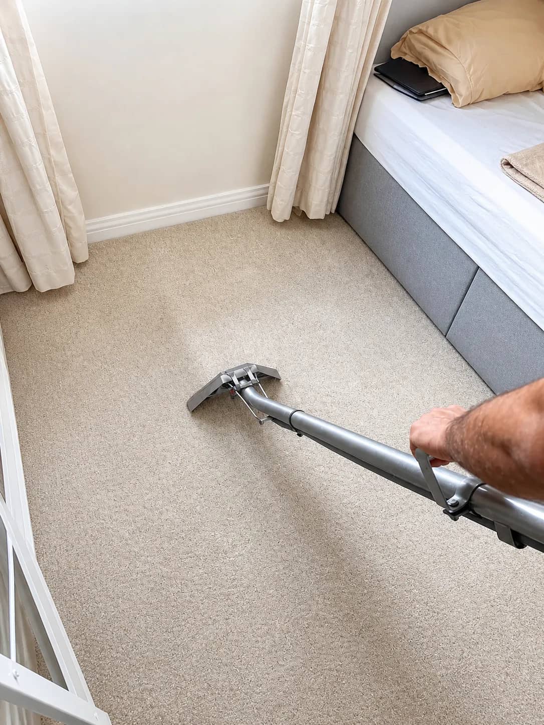 Carpet cleaning extraction wand in use on a light carpet near a radiator.